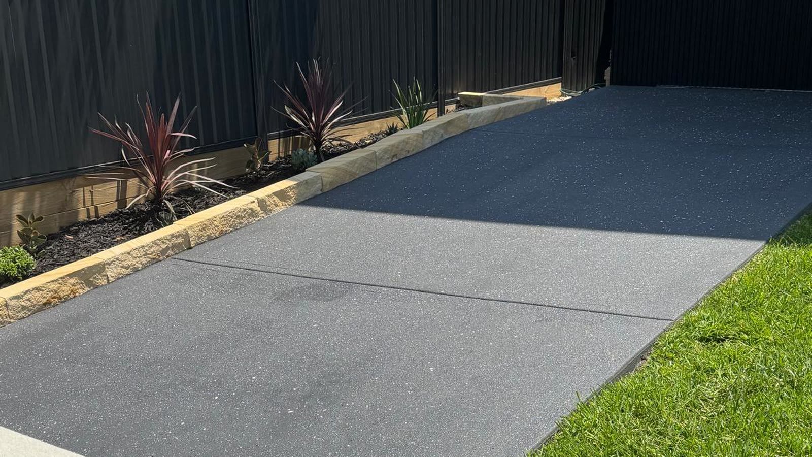 Charcoal spray-crete driveway and path beside a garden bed